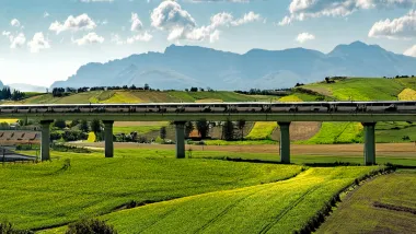 AI-generated image of high-speed rail trail in elevated track in green hilly farmland.
